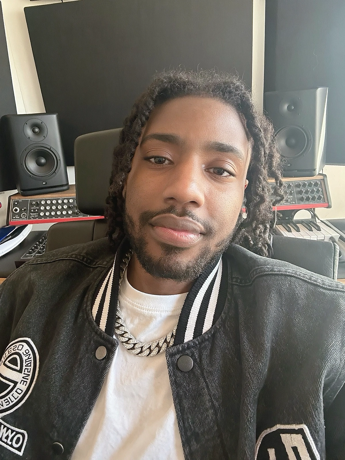 Close shoulder-up candid portrait of a fictional young adult hip-hop / rap artist smiling naturally in their own music recording studio
